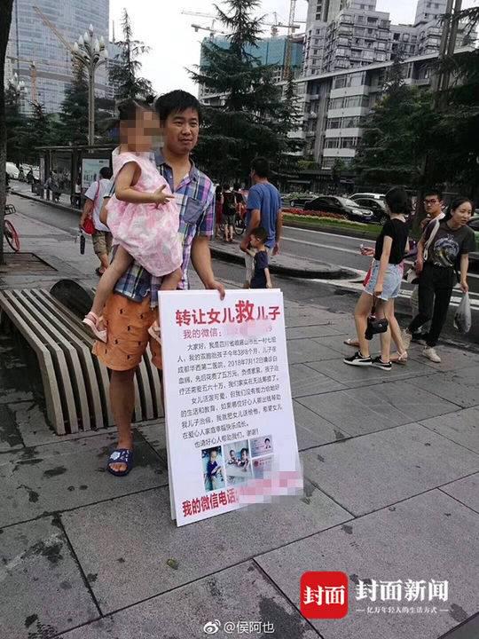 梁育佳站在街头，怀里抱着女儿，面前放着一块牌子：“转让女儿救儿子。”