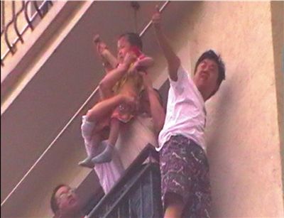 成功救出男童，施救者向楼下围观者挥手示意。